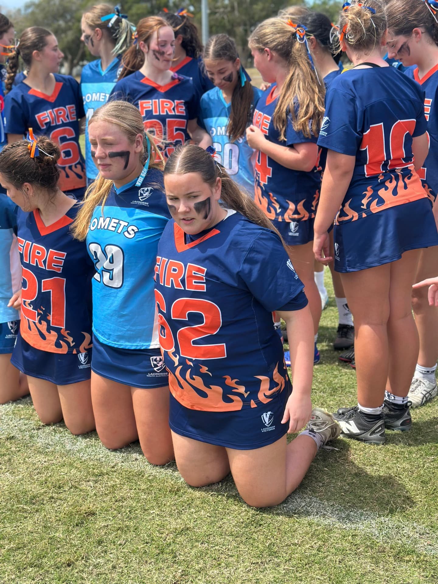 Ivy, in her FIRE #62 jersey, kneeling with teammates and players from the Comets after a match.